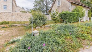 A stone building with a traditional design, a garden with various plants and flowers, and a clear sky.