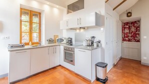 A compact kitchen with white cabinets, a microwave, a kettle, and a trash bin.