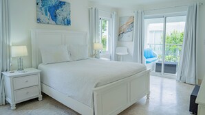 Un dormitorio con una cama grande, una mesita de noche, una lámpara y vistas al balcón exterior.