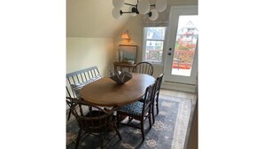 Uma sala de jantar com uma mesa redonda, quatro cadeiras, um tapete e uma porta com vista para uma casa e uma construção vermelha lá fora.