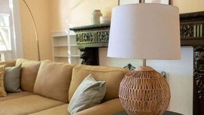 Un divano beige con cuscini, un tavolino con lampada in fibra naturale e una mensola decorativa sullo sfondo.