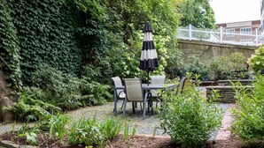 Un patio giardino con tavolo e sedie, immerso nel verde e delimitato da un recinto bianco.