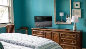 Camera da letto con pareti color acquamarina, una cassettiera in legno, una televisione e un letto con lenzuola a righe.