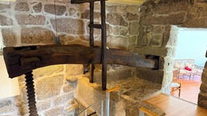 A stone interior with a wooden beam structure, a staircase, and a view of a room with a sofa and a table. - Charming Stone Retreat on 19ha Private Estate | Valley Views & Total Privacy (Salvador do Monte)