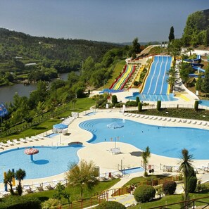 A large swimming pool with a water slide, surrounded by lounge chairs and palm trees.