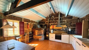 A rustic kitchen with stone walls, wooden beams, a stone fireplace, and a wooden table. - Charming Stone Retreat on 19ha Private Estate | Valley Views & Total Privacy (Salvador do Monte)