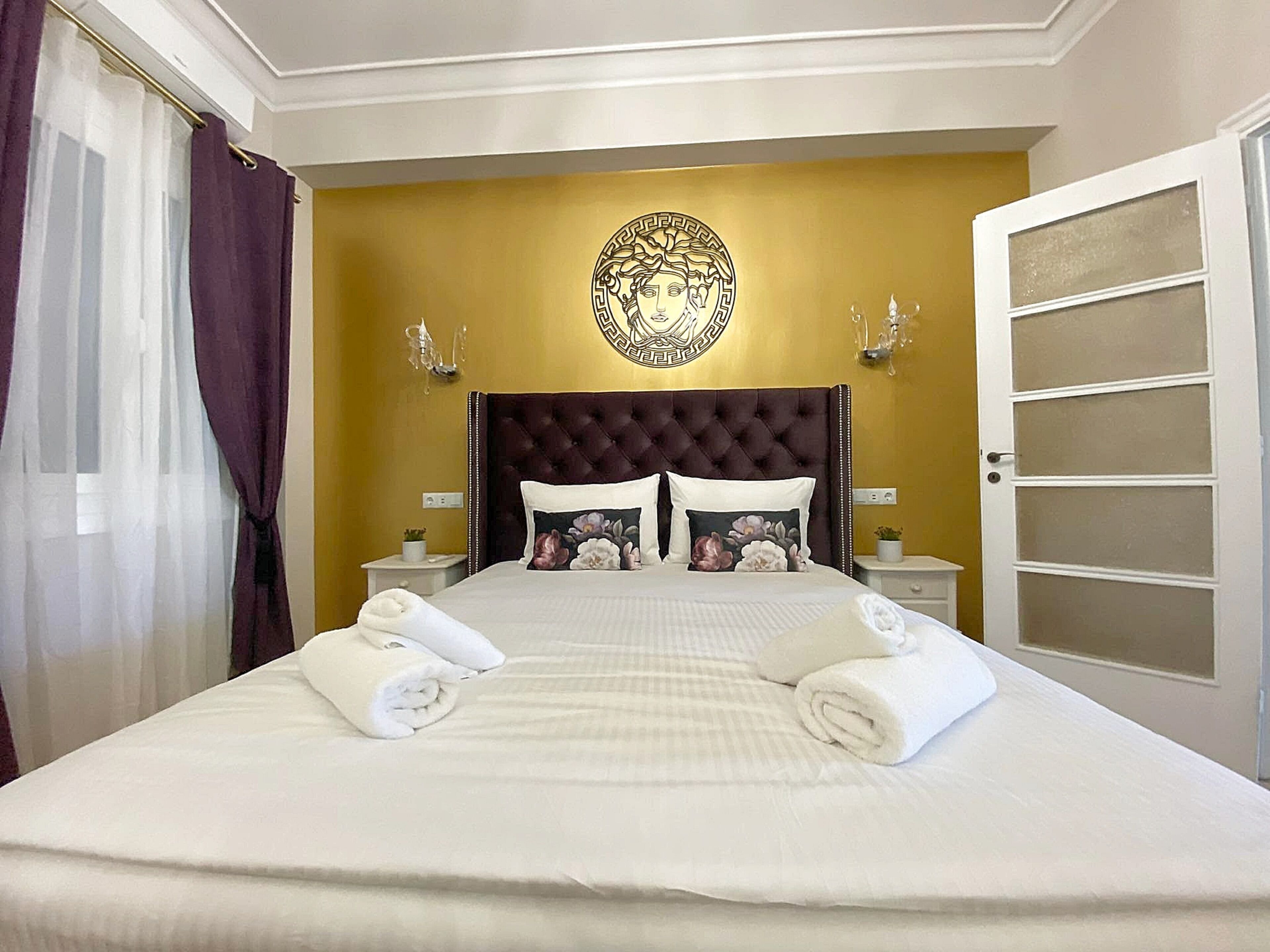 A hotel room with a large bed, a decorative wall piece, two bedside tables with lamps, and a view of the outside.