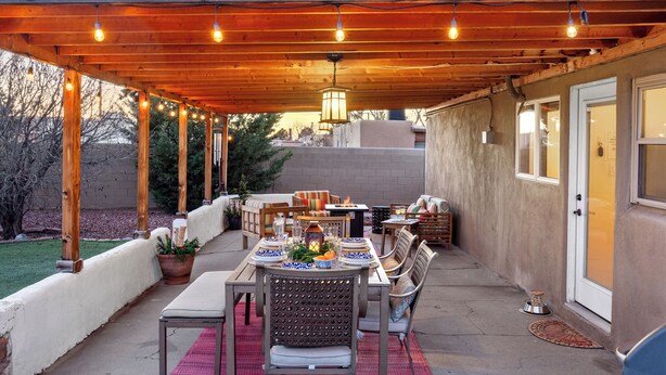 Patio esterno con pergola in legno, luci a stringa e tavolo da pranzo con sedie.
