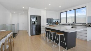 A modern kitchen with a central island, bar stools, and a large window. - Beachside Living with Sea Views at the Pines (Ocean Grove)