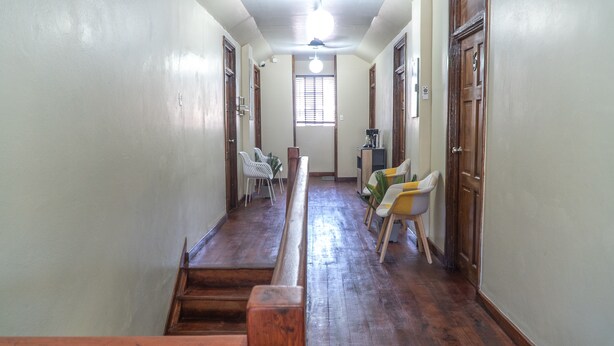 A hallway with wooden flooring, white walls, and a ceiling fan. There are chairs and a table in the distance, and a window with blinds. - Chillinn at Duke (Kingston)