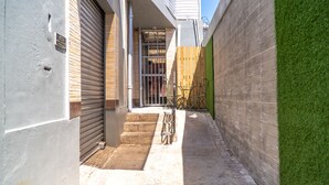 A narrow alleyway with a closed metal shutter door, a wooden fence, and a small set of steps leading to a gated entrance. - Chillinn at Duke (Kingston)