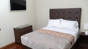 A neatly arranged hotel room with a bed, a bedside table, a TV mounted on the wall, and a small nightstand with a lamp. - Chillinn at Duke (Kingston)