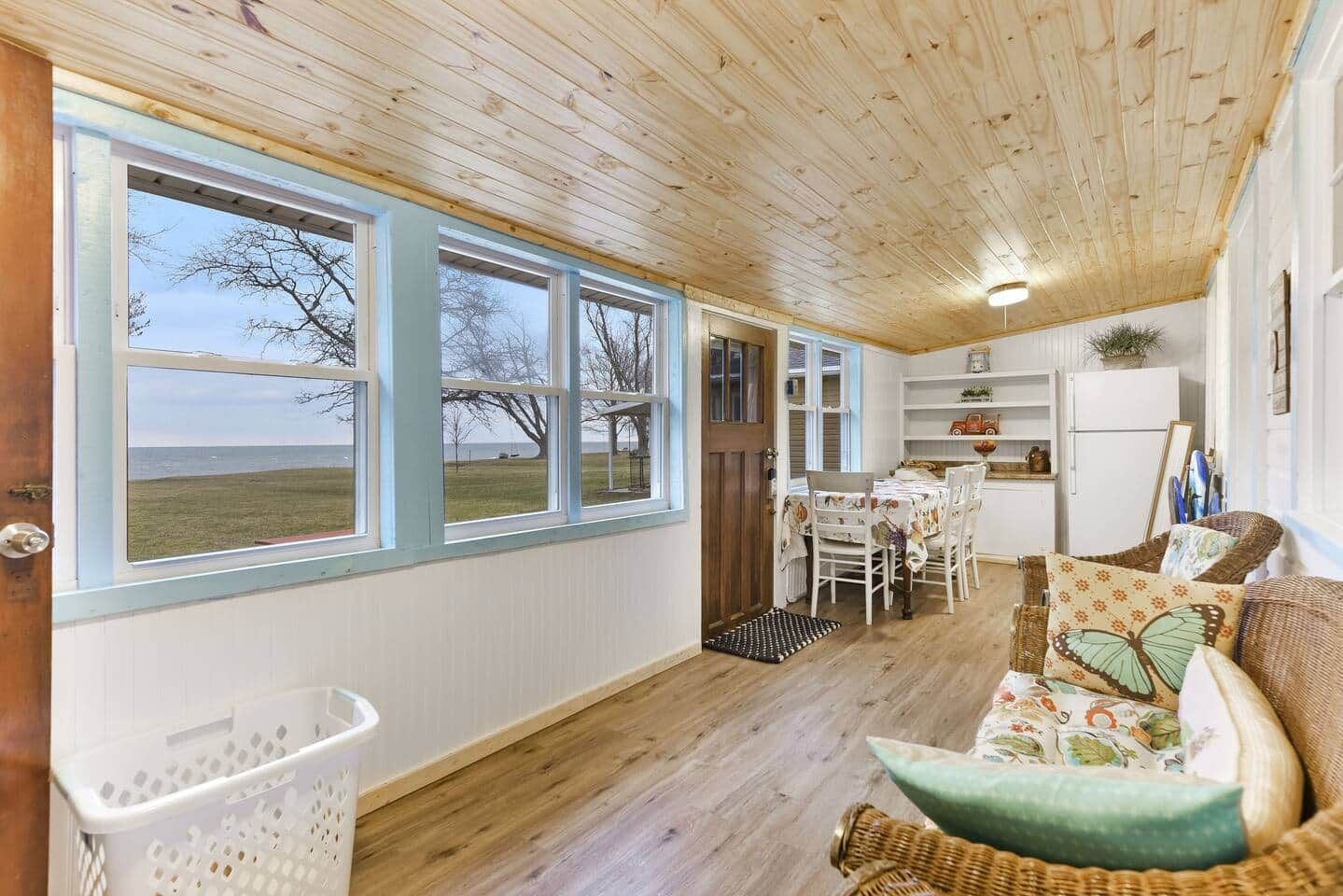 A cozy interior with a wooden ceiling, a dining area with a table and chairs, and a view through large windows.
