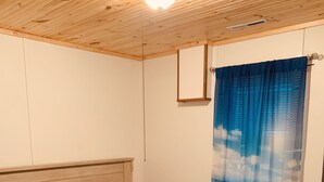 Een slaapkamer met een houten plafond, een bed met een beige en blauwe sprei, en een raam met blauwe gordijnen.