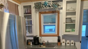 Een keuken met witte kasten, een roestvrijstalen koelkast, een raam met uitzicht en een decoratieve bloemstuk erboven.