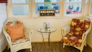 Een gezellige kamer met twee rieten stoelen, een klein glazen tafeltje en een bordje met de tekst 'Welcome to the Cottage'.
