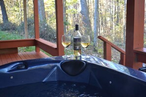A hot tub with a bottle and glasses of white wine on a wooden deck with a forest view. - 7BR/3BA Cabin, HOT TUB, game room (Logan)