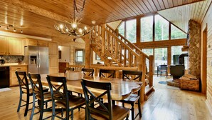A wooden cabin interior with a dining area, kitchen, and a stone fireplace. - Private Lake Resort: large yard, sandy beach, pontoon, fire pit, home theater (Spooner)