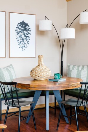 Een ronde houten tafel met een gevlochten vaas en een mok, omringd door zwarte stoelen met blauwe accenten.