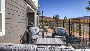 Un patio con mobiliario exterior, una parrilla y vistas a un paisaje montañoso.