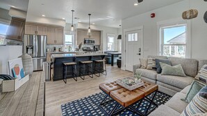 Una cocina moderna con electrodomésticos de acero inoxidable, una isla central con taburetes y una zona de estar acogedora con sofá y mesa de centro.