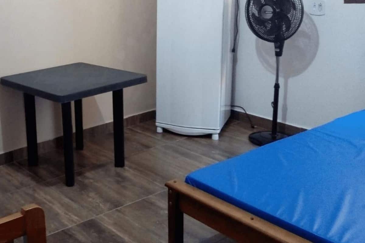 A small room with a bed, a table, and a fan.