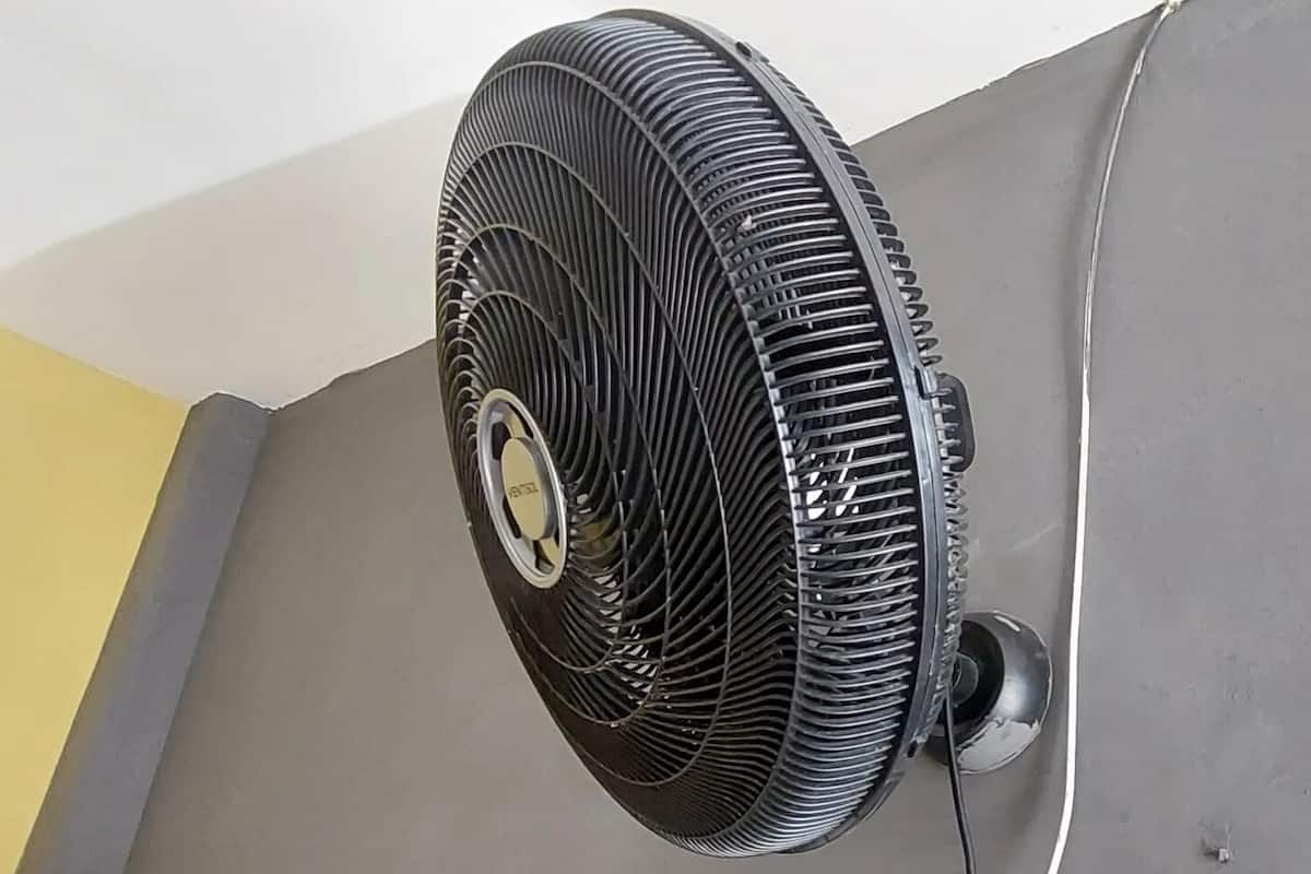 A standing fan mounted on a wall, with a visible power cord.