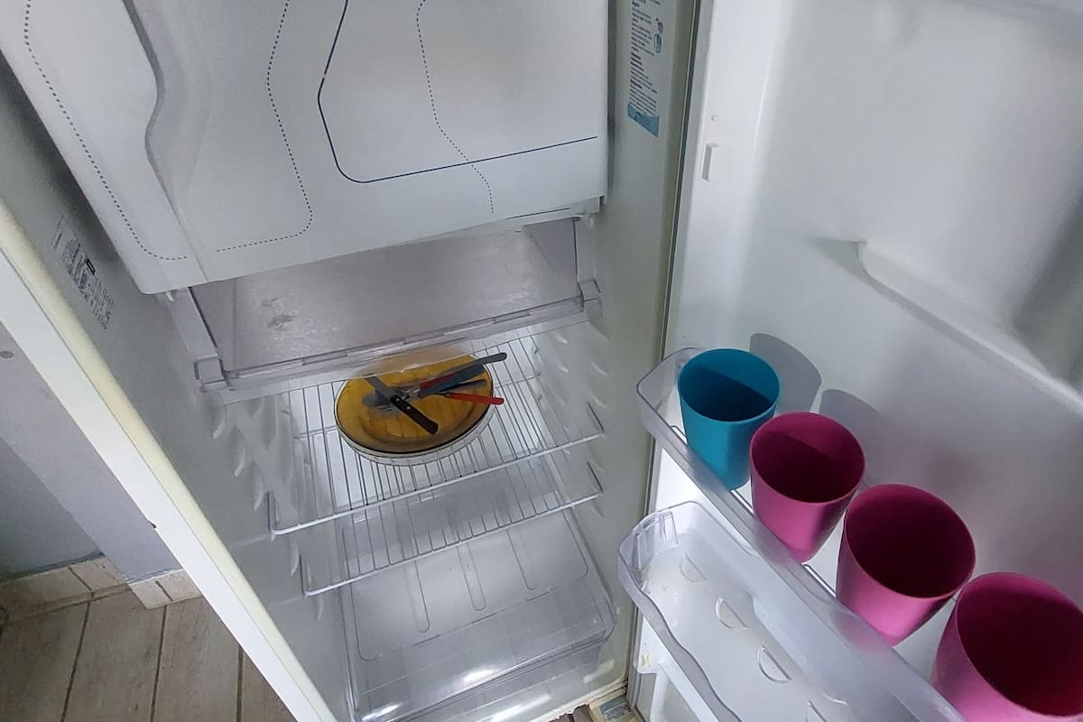 An open refrigerator with a clear shelf, a yellow container, and several colorful cups.
