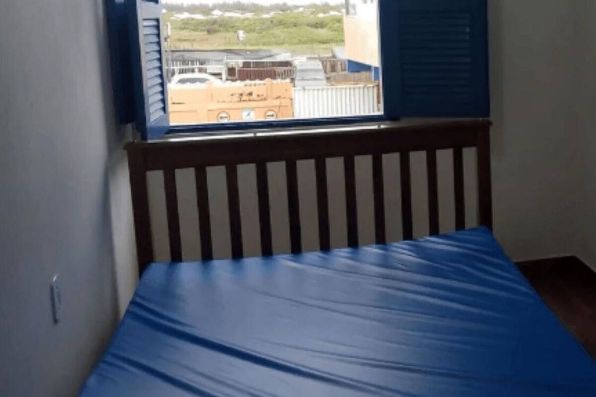 A small room with a single bed, a window with a view of buildings, and a door leading to a bathroom.