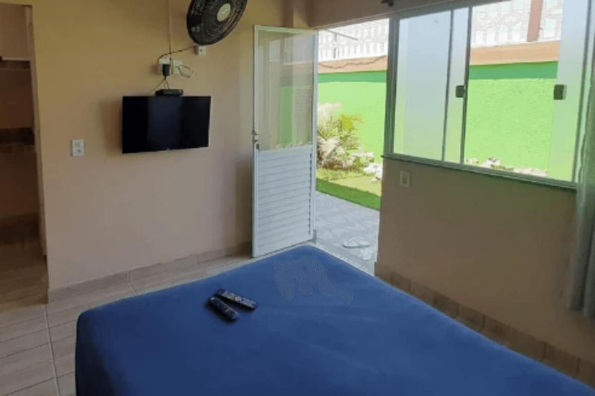 A room with a bed, a TV mounted on the wall, and a view of a green outdoor area through a sliding door.