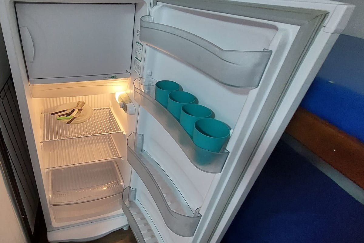 A refrigerator with a water dispenser, a shelf with utensils, and a shelf with teal cups.