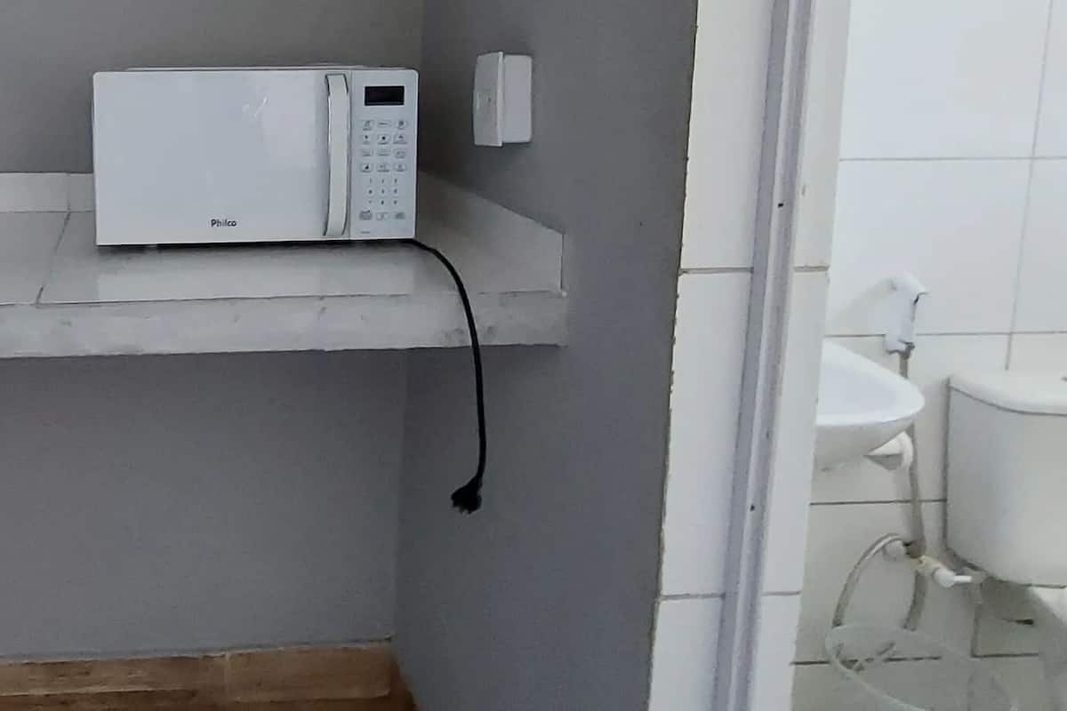 A small bathroom with a white toilet, a white sink, and a white microwave on a shelf.