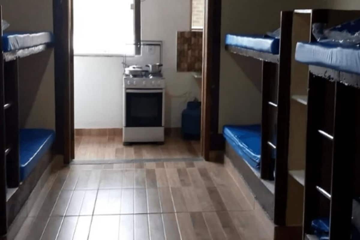 A narrow hallway with bunk beds on both sides, a kitchenette area with a stove and microwave, and a small window providing natural light.