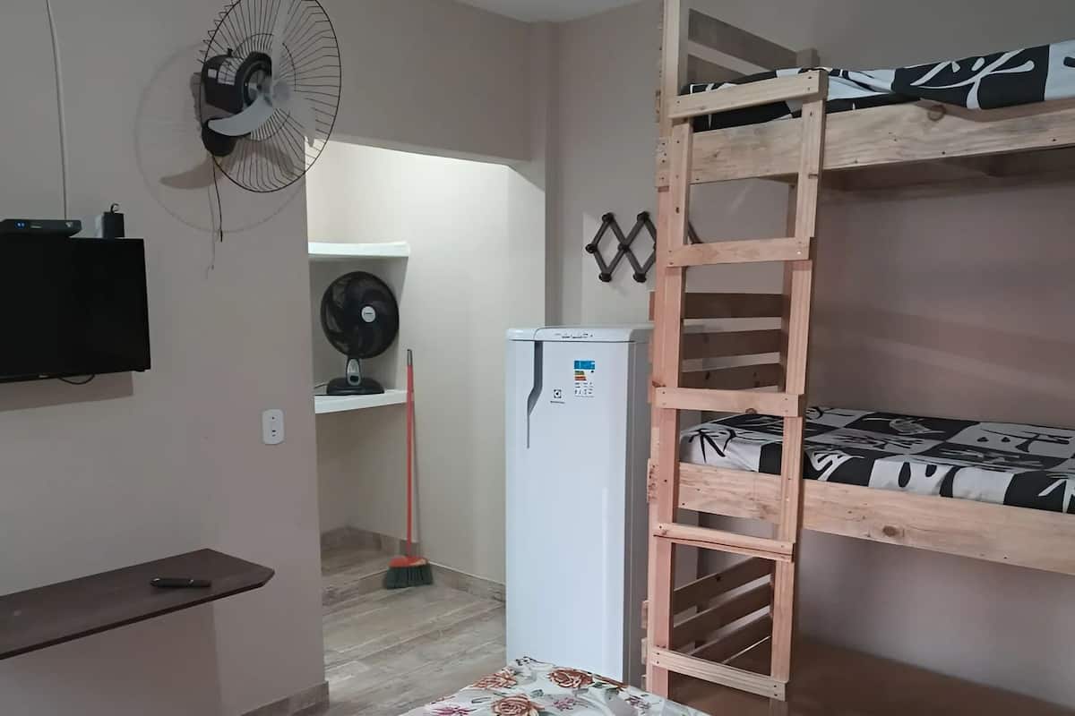 A room with a bunk bed, a TV, a fan, a refrigerator, and a broom.