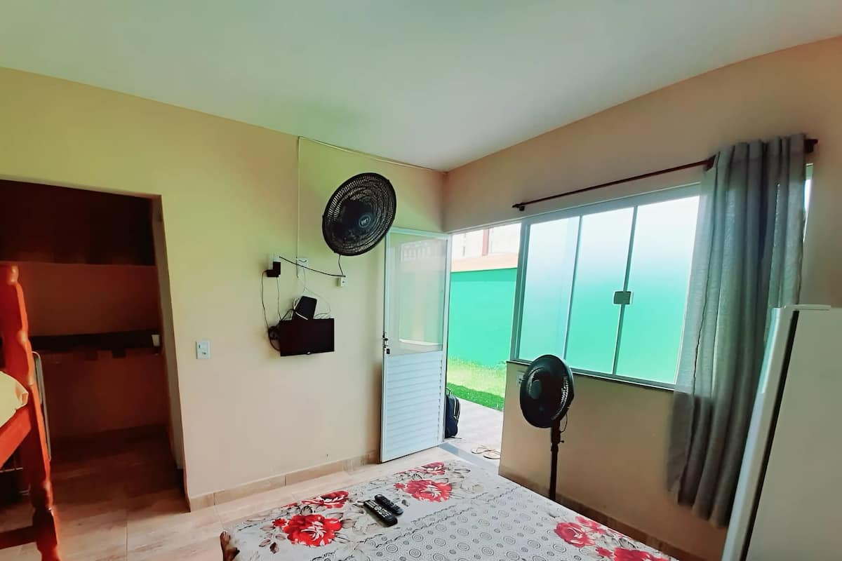 A bedroom with a bed, a wooden chair, a fan, and a window with curtains.