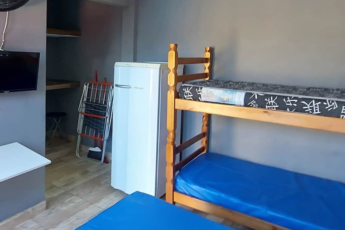A compact room with a bunk bed, a small desk, a TV mounted on the wall, and a refrigerator.
