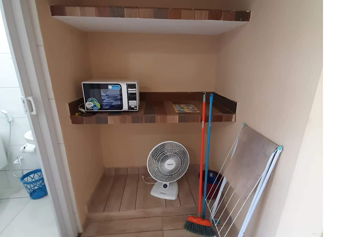 A small bathroom with a microwave on a shelf, a fan on the floor, and a broom leaning against the wall.