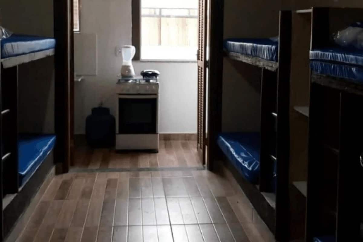 A dormitory room with bunk beds, a small kitchenette, and a window.
