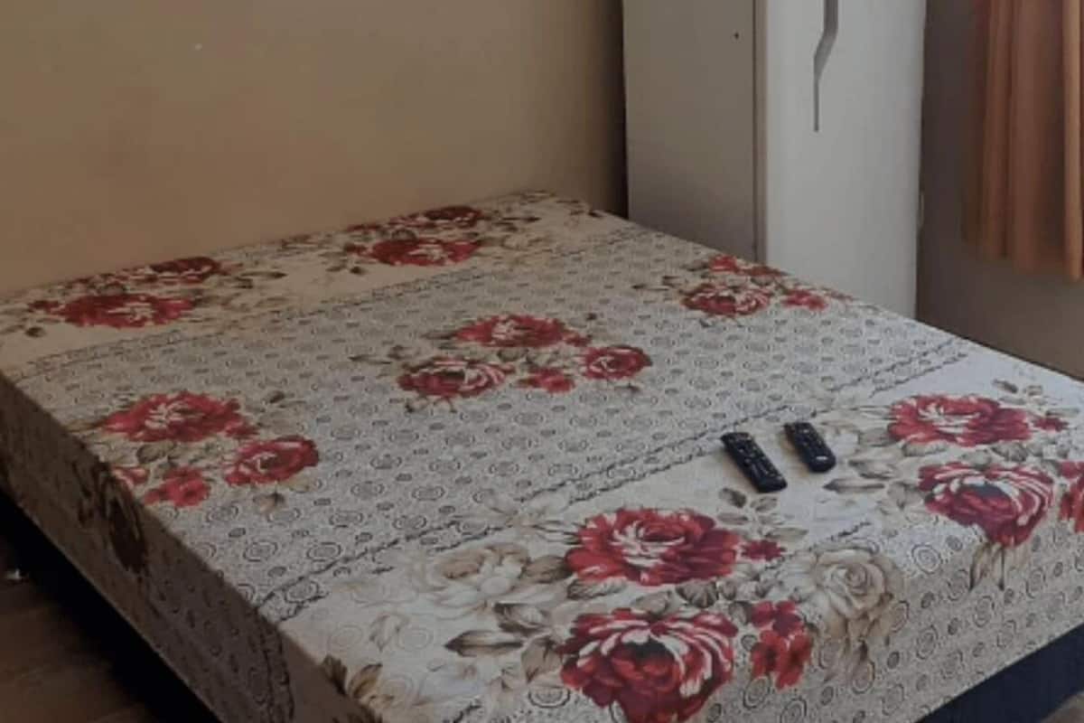 A room with a bed covered in floral bedding, a window with curtains, and a door with a handle.