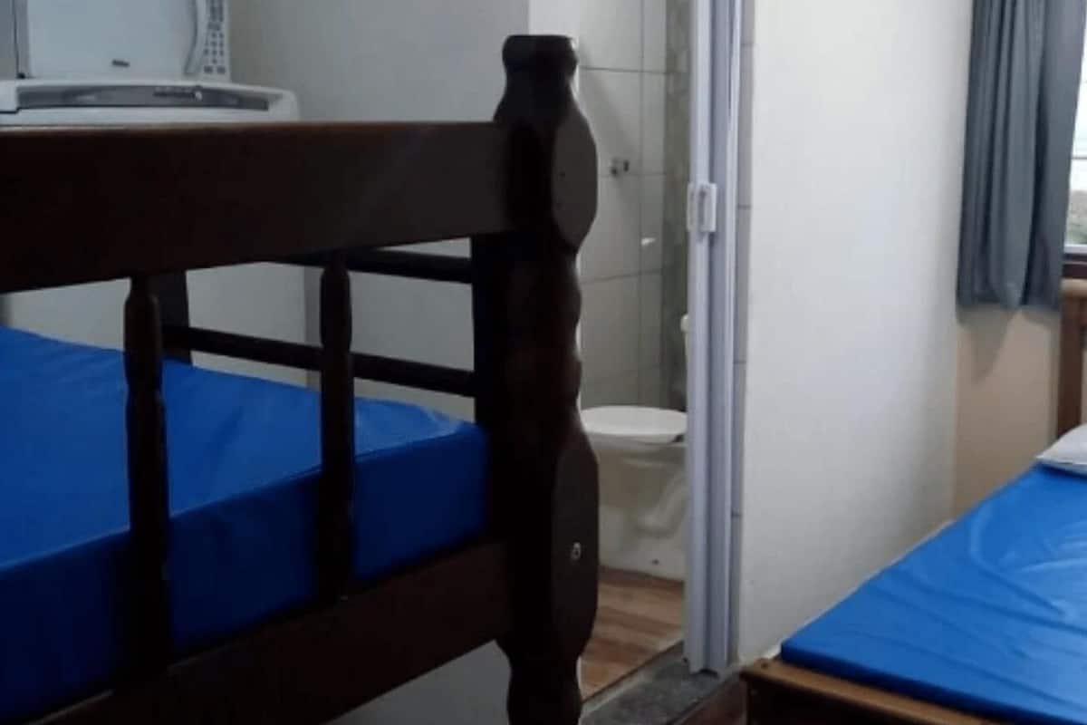 A room with a wooden bunk bed, a single bed, a window with a view, and a toilet.
