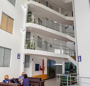 Vestíbulo de hotel de varios niveles con una escalera central, zonas de estar y un ventanal grande.