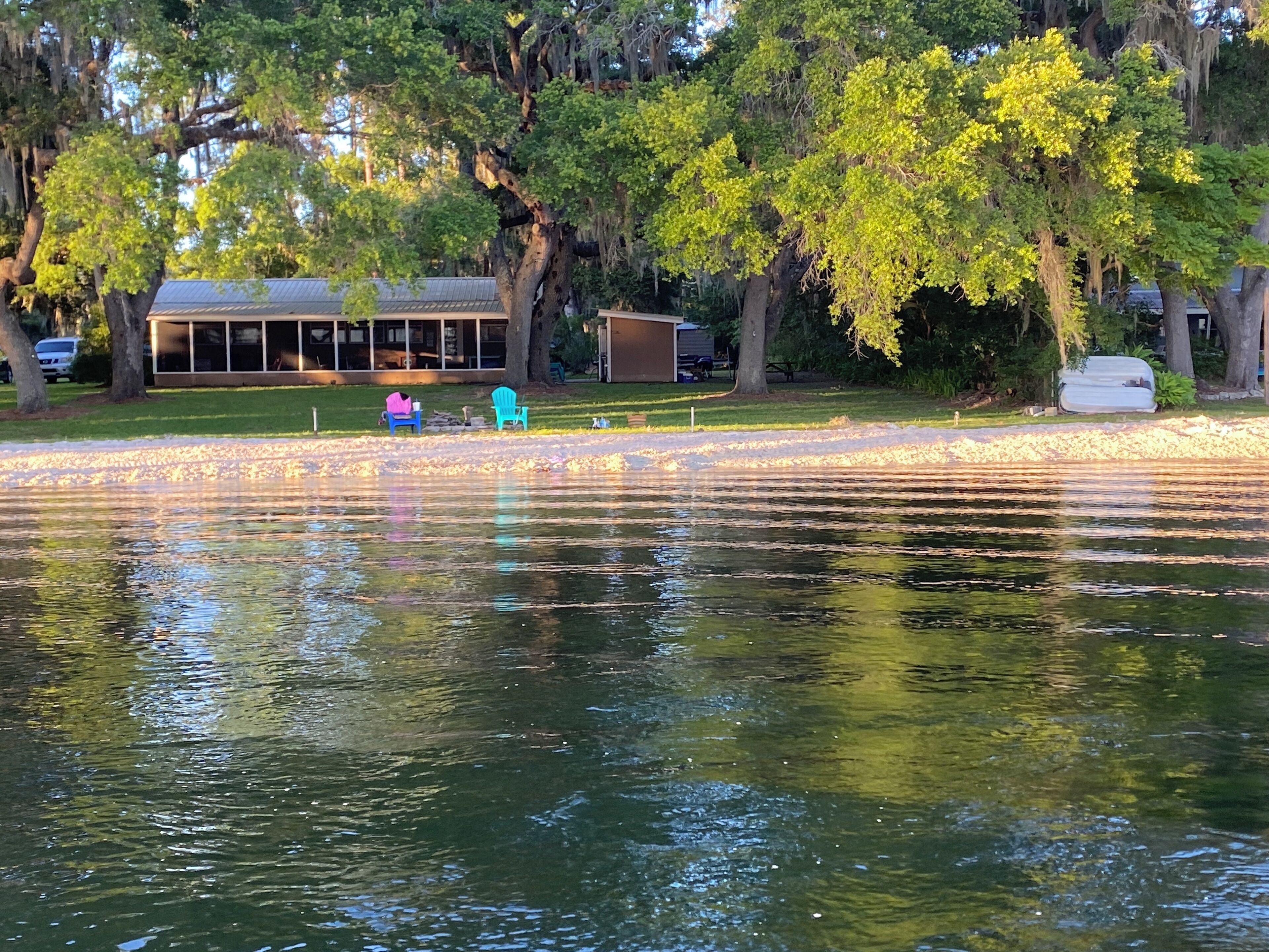 A lakeside view with a building, outdoor seating, and a covered area.