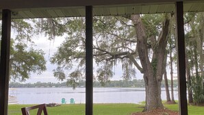 A room with large windows overlooking a lake, a chair, and a table.