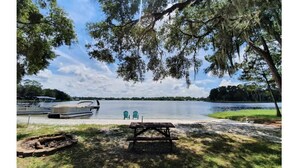 A lakeside picnic area with a bench, two chairs, and a boat dock.