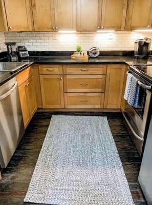 Kitchen features a range hood, cabinets, and a countertop, with a rug and a small plant.