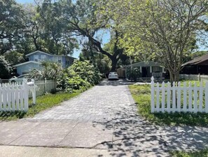 Drive up to a charming home surrounded by lush greenery and a picturesque white picket fence.