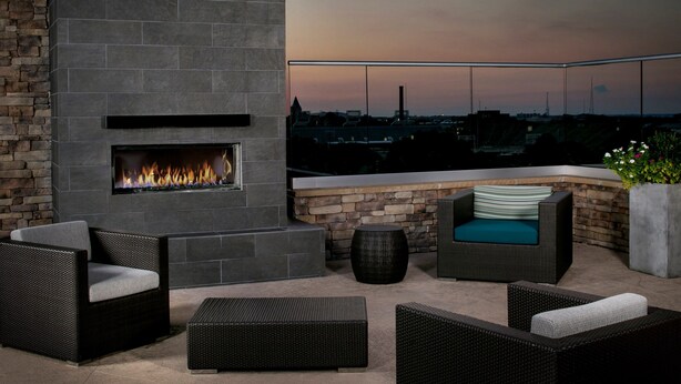 A rooftop patio with a stone fireplace, wicker furniture, and a view of the cityscape at dusk.