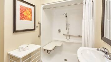 A bathroom with a shower, sink, and framed artwork.