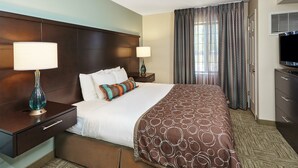 Une chambre d’hôtel avec un grand lit, deux tables de chevet avec des lampes, une télévision et une fenêtre avec des rideaux.