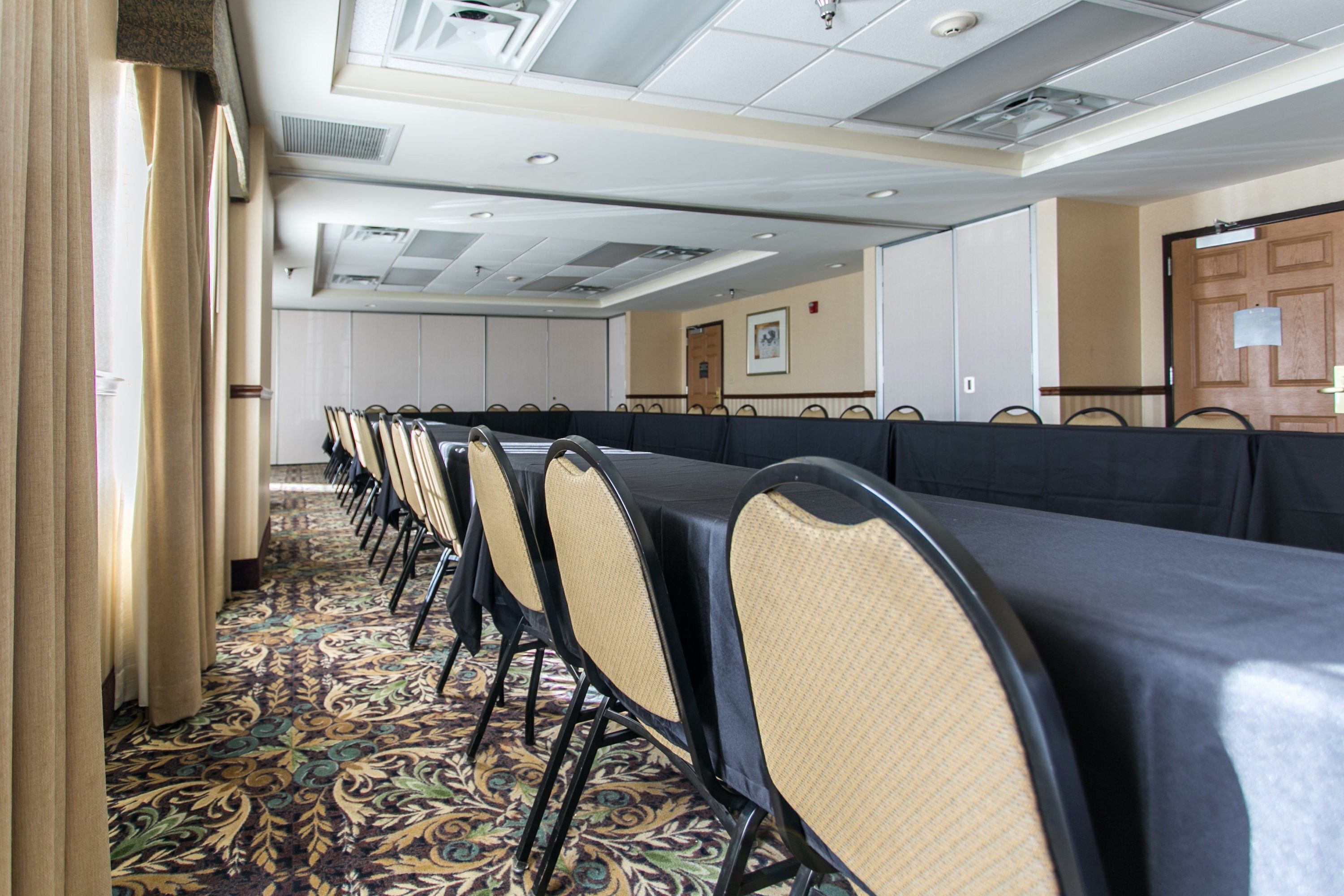 Une salle de conférence avec une longue table et des chaises, un sol recouvert de moquette et une porte au fond.